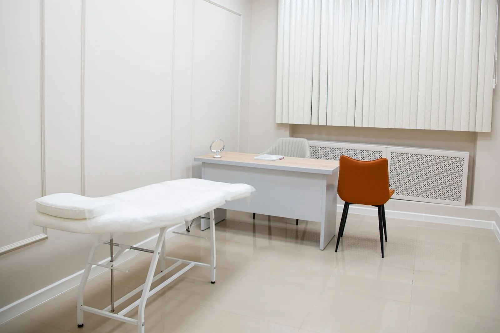 A calm, modern treatment room — cream panelling, a clean white couch and a light-wood consultation desk